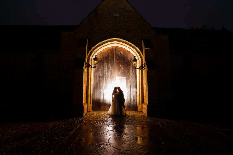 Dramatic backlit silhouette of wedding couple in the Great Tithe Barn entrance archway at night